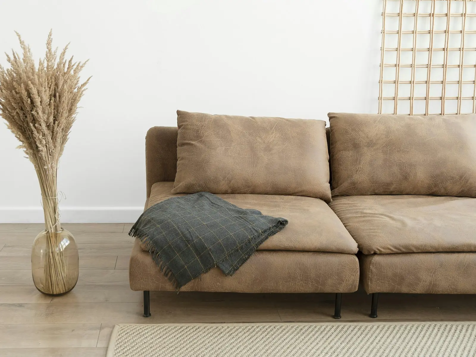A wool throw on a tan sofa beside a vase of dried grasses