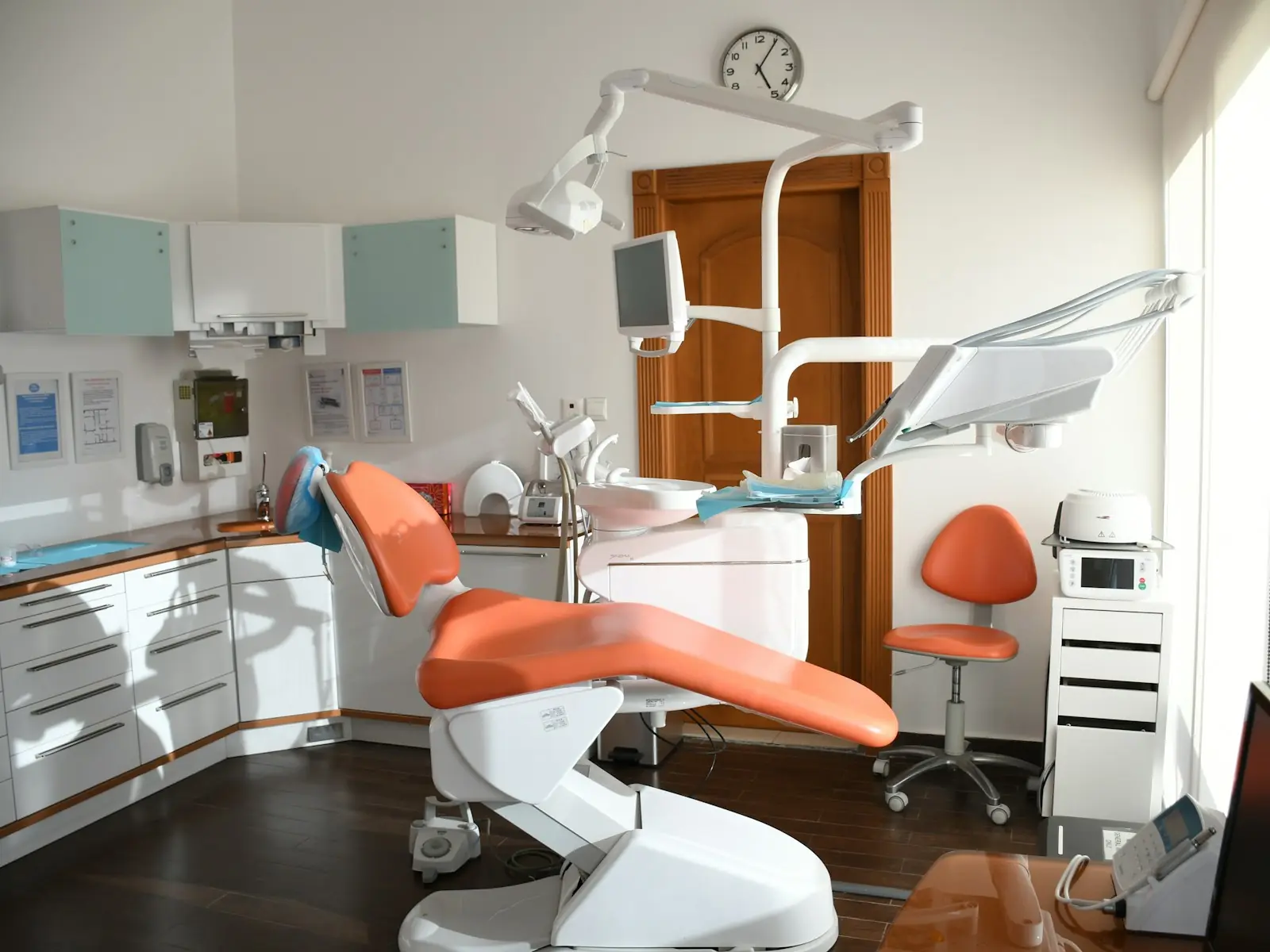 A bright dental treatment room with an orange patient chair